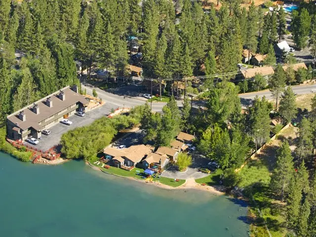 The image shows an aerial view of a resort situated on the shore of a lake, surrounded by trees,...