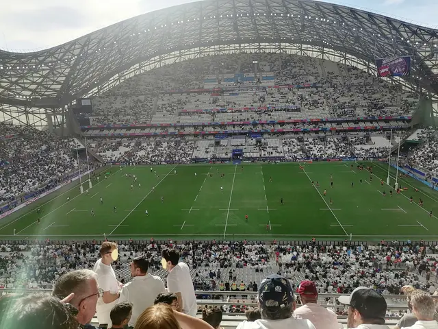 The image shows a large stadium filled with lots of people watching a rugby game. The stadium is...
