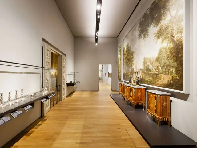 The image shows a room filled with lots of art on display, including paintings on the walls,...