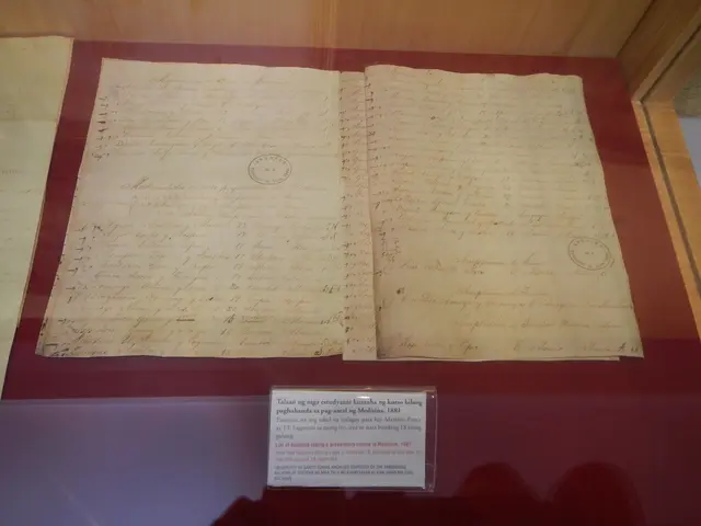 The image shows an old document in a glass case on display in a museum. The document appears to be...