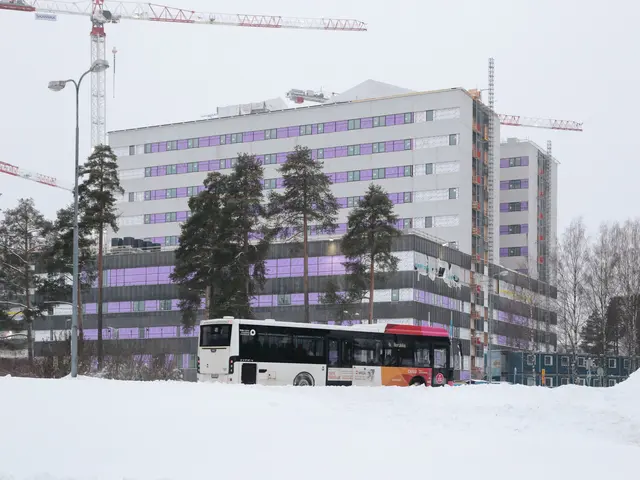 The image shows a bus driving down a snow-covered street next to tall buildings, with trees, light...