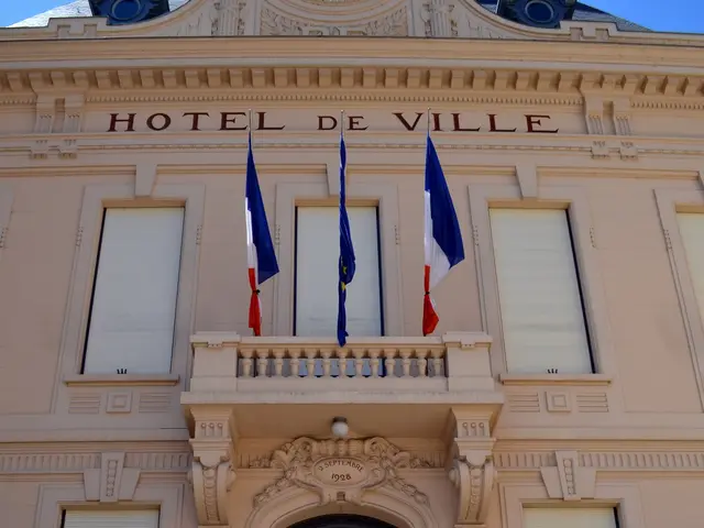 The image shows the Hotel de Ville in Cannes, France. It is a building with windows, a door, flags,...