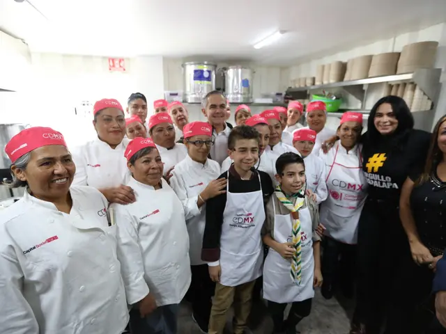 The image shows a group of people standing in a kitchen, smiling and posing for a photo. Some of...