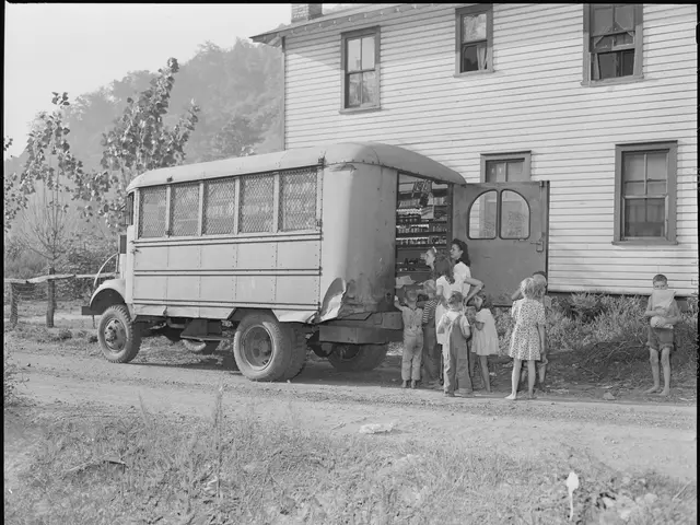 The image shows a black and white photo of a group of children standing in front of a school bus....