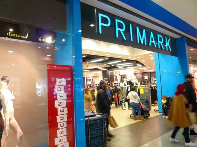 The image shows a Primark store in a shopping mall with people walking past it. There are...