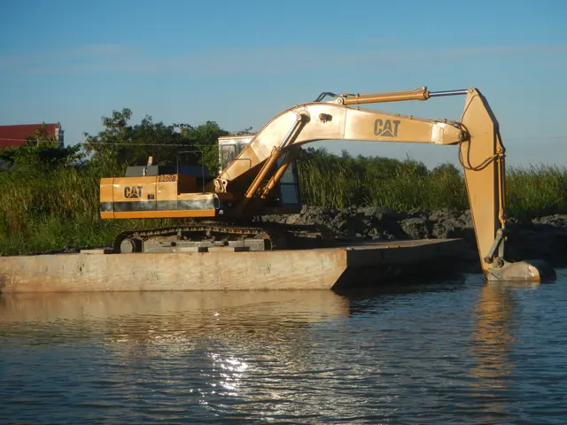 The image shows an excavator on a barge in the water, surrounded by rocks, plants, trees, and a...