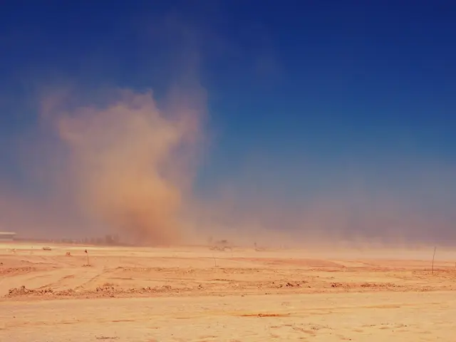 The image shows a dust storm in the middle of a desert, with sand on the ground and a building in...