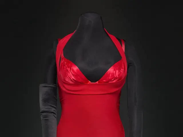The image shows a mannequin wearing a red dress and black gloves against a black background. The...
