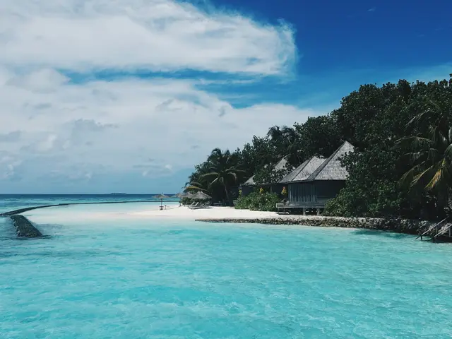 The image shows a stunning view of a beach with crystal clear blue water, white sand, lush green...