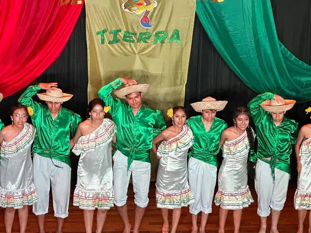 The image shows a group of people standing on top of a wooden floor, wearing traditional Mexican...