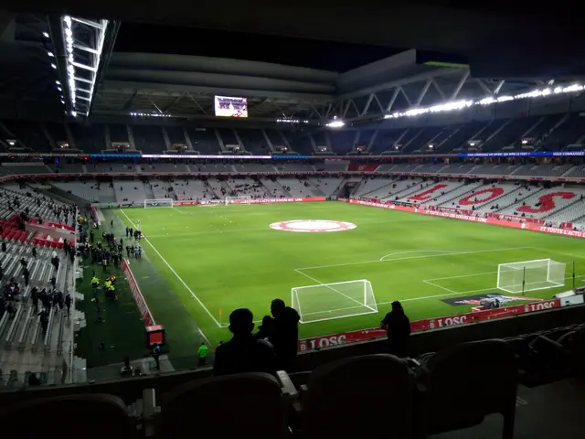 The image shows a large stadium filled with lots of people watching a soccer game. The stadium is...