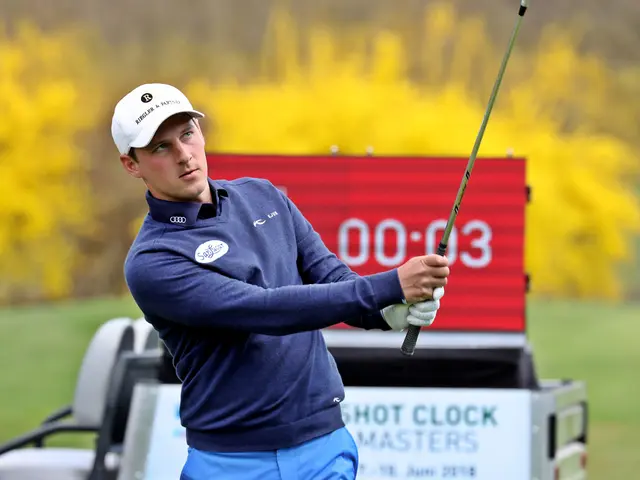 The image shows a man wearing a blue t-shirt and blue pants, swinging a golf club on top of a green...