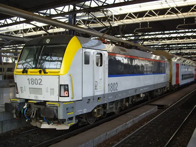 The image shows a diesel-electric locomotive traveling down train tracks next to a platform, with...