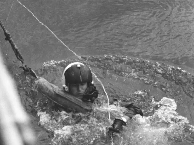 The image shows a man in a wet suit and helmet floating in the water, with a rope attached to his...