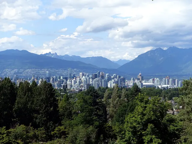 The image shows a view of the city of Vancouver from the top of a hill, with trees in the...
