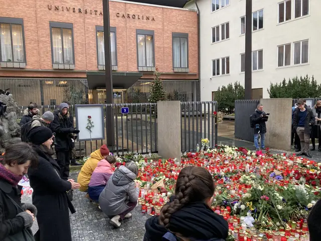The image shows a group of people standing around a bunch of flowers and candles placed on the...