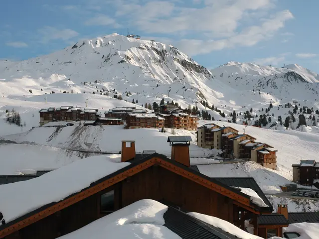 The image shows a picturesque view of a ski resort with snow-covered mountains in the background....