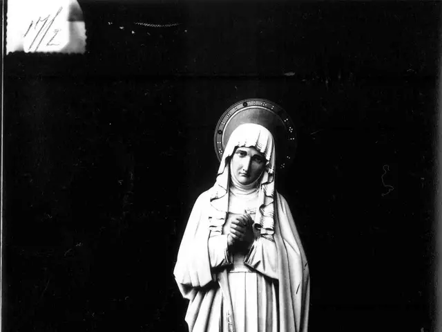 The image shows a black and white photo of a statue of Our Lady of Fatima, with her hands clasped...