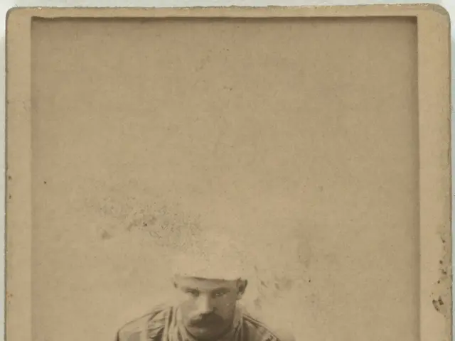 The image shows an old black and white photo of a baseball player kneeling on the ground, holding a...