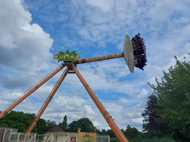 The image shows a roller coaster ride in the middle of a park, surrounded by a metal fence and a...