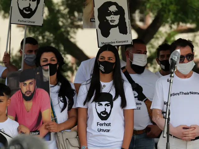 The image shows a group of people wearing masks and holding signs in front of a crowd, with a...