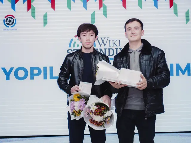 The image shows two men standing next to each other on a stage, both wearing black jackets and...