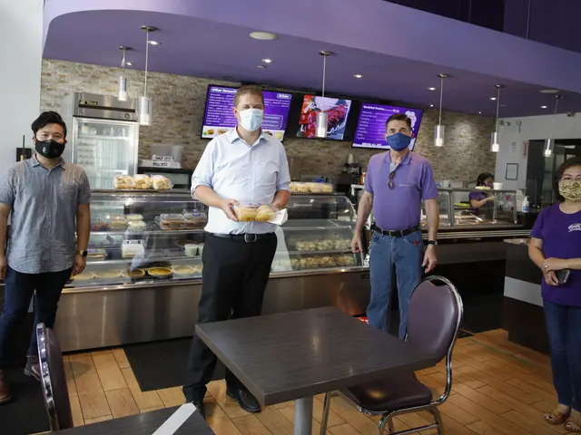 The image shows a group of four people wearing face masks standing in front of a counter in a...
