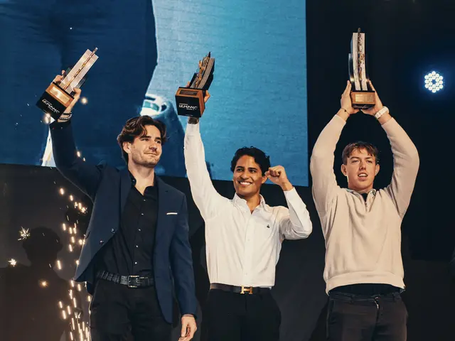 The image shows three men standing on a stage, each holding up a trophy in celebration. The man on...