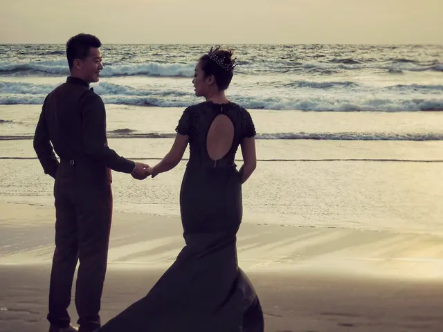 The image shows a bride and groom holding hands on the beach at sunset. The sky is a beautiful mix...