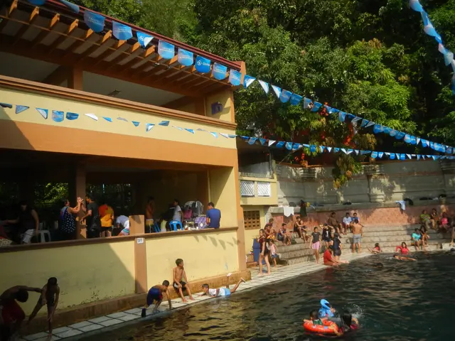 The image shows a group of people swimming in a pool in front of a building, with some people...