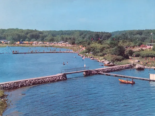 The image shows an old photo of a lake with a boat in the water, a bridge with railings, flags with...