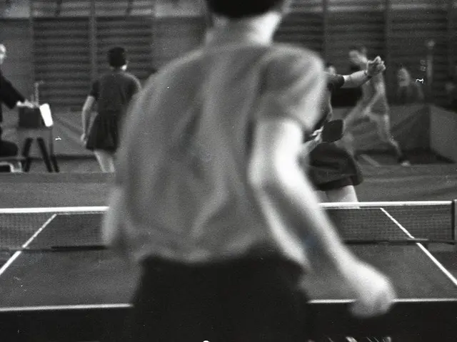 The image shows a group of people playing ping pong on a court, with a net in the middle and a wall...