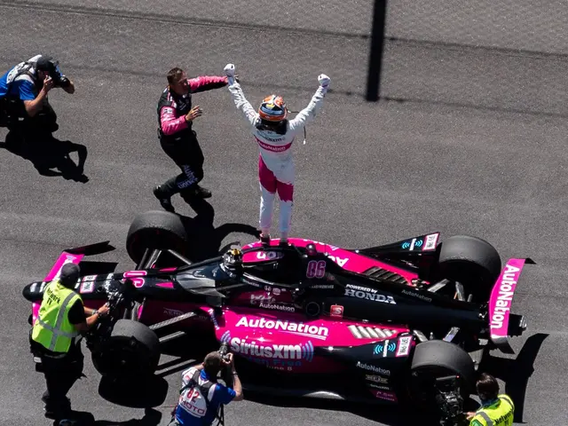The image shows a man standing on top of a pink race car, wearing a helmet and gloves, surrounded...