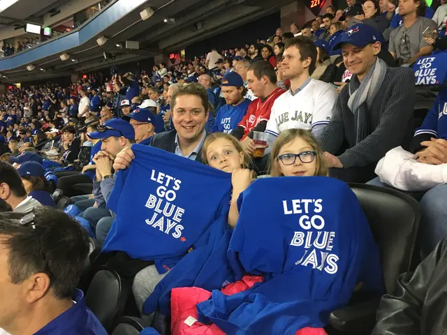The image shows a group of Toronto Blue Jays fans sitting in the stands at a baseball game, wearing...