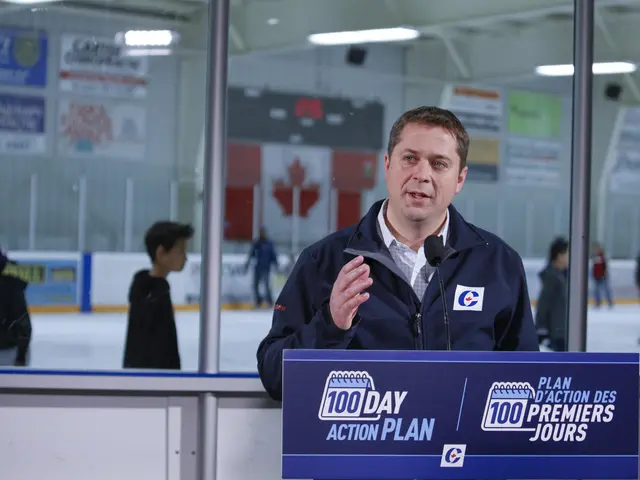 The image shows a man standing at a podium in front of a hockey rink, wearing a jacket and speaking...