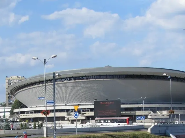 The image shows a large stadium with a lot of traffic in front of it, surrounded by buildings,...