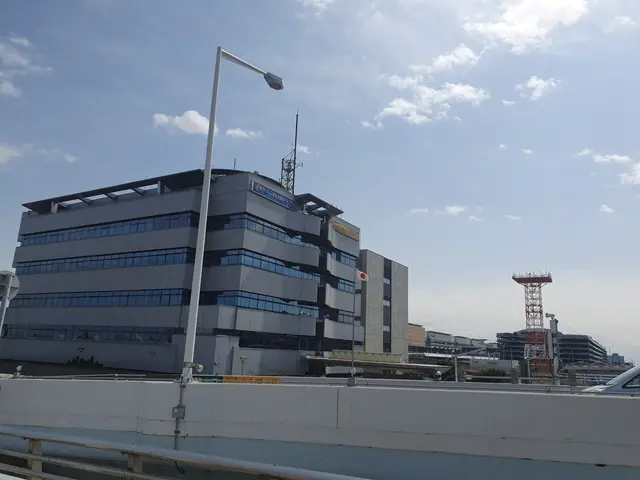 The image shows a large building with a lot of windows on top of it, surrounded by street poles,...