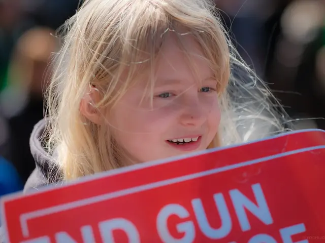 The image shows a young girl with a bright smile on her face, holding a red sign that reads "End...