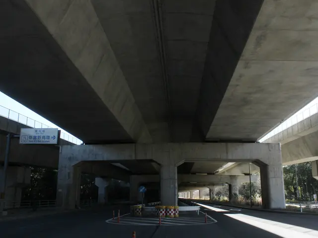 The image shows a highway under a bridge with traffic cones on the side of it. The road is lined...