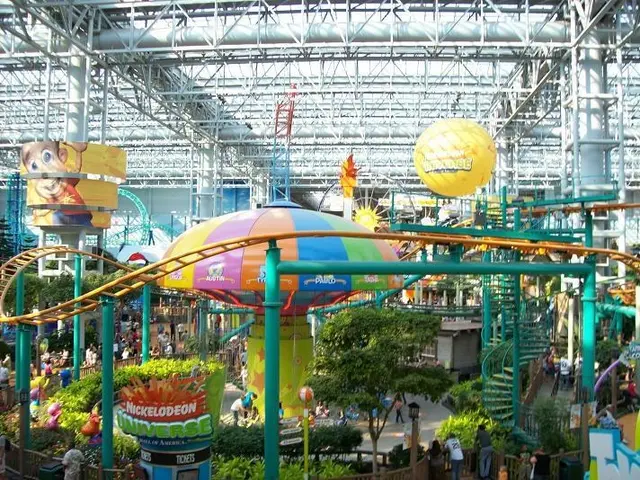 The image shows a large indoor water park with a roller coaster in the middle of it. There are many...
