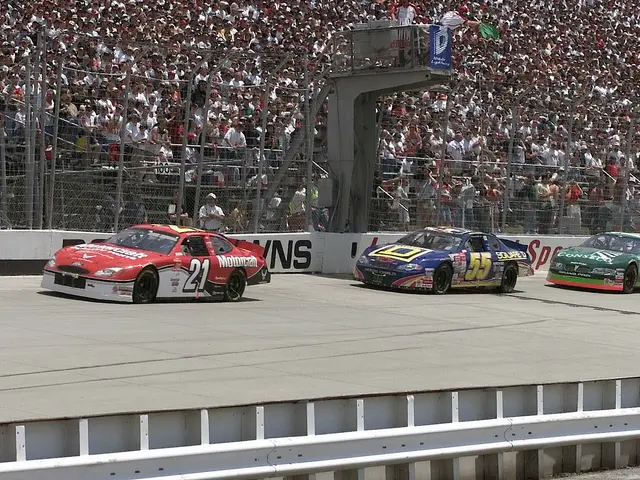 The image shows three NASCAR cars racing down a race track in front of a large crowd. The cars are...