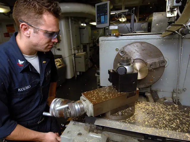The image shows a machinist wearing glasses and working on a machine in a factory. In the...