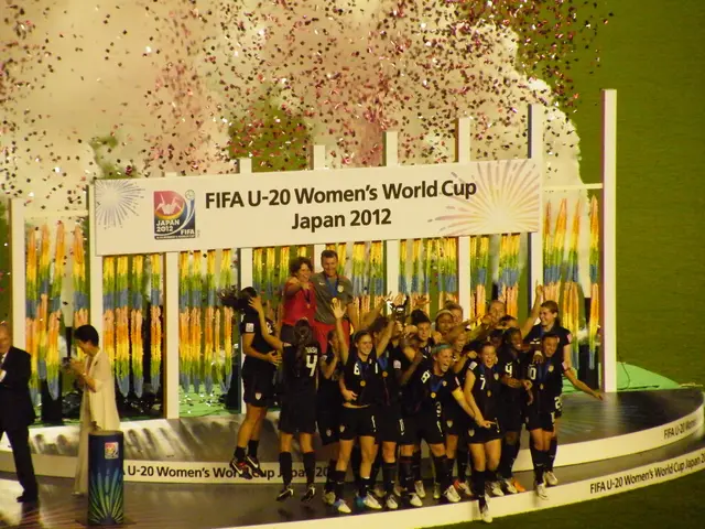 The image shows a group of women's soccer players standing on top of a stage, celebrating their...