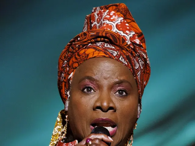 The image shows a woman in an orange and blue dress singing into a microphone, with a blurred...