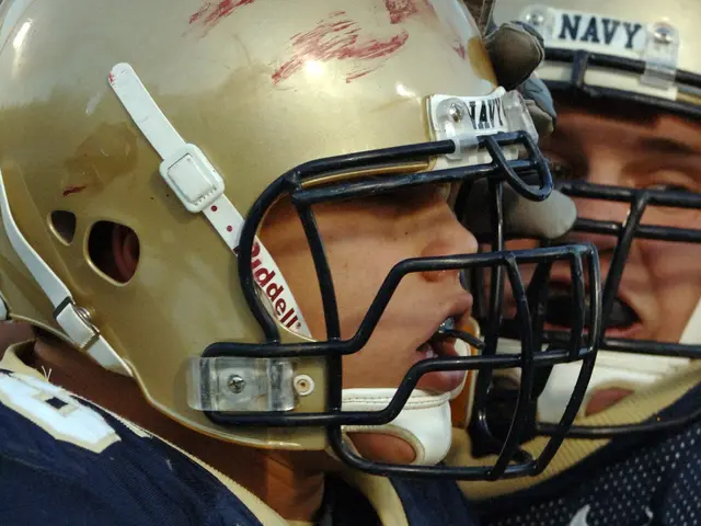 The image shows two football players wearing navy blue uniforms and helmets, embracing each other...