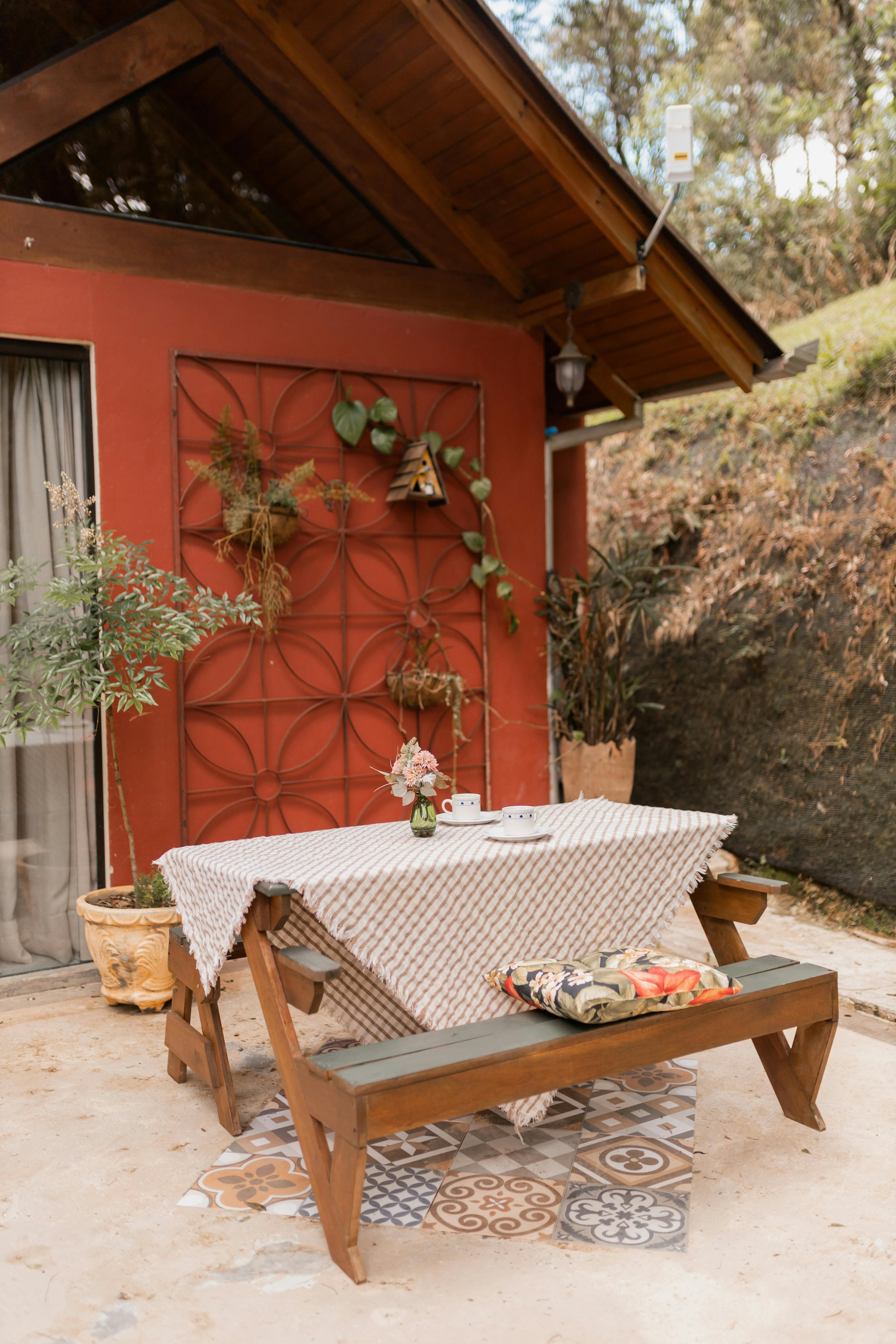 Outdoor table, decorated with greenery, located beside a striped outdoor chair with a plush cushion. Outdoor table with textured surface and a potted plant, situated alongside a plush patio chair adorned with a patterned cushion