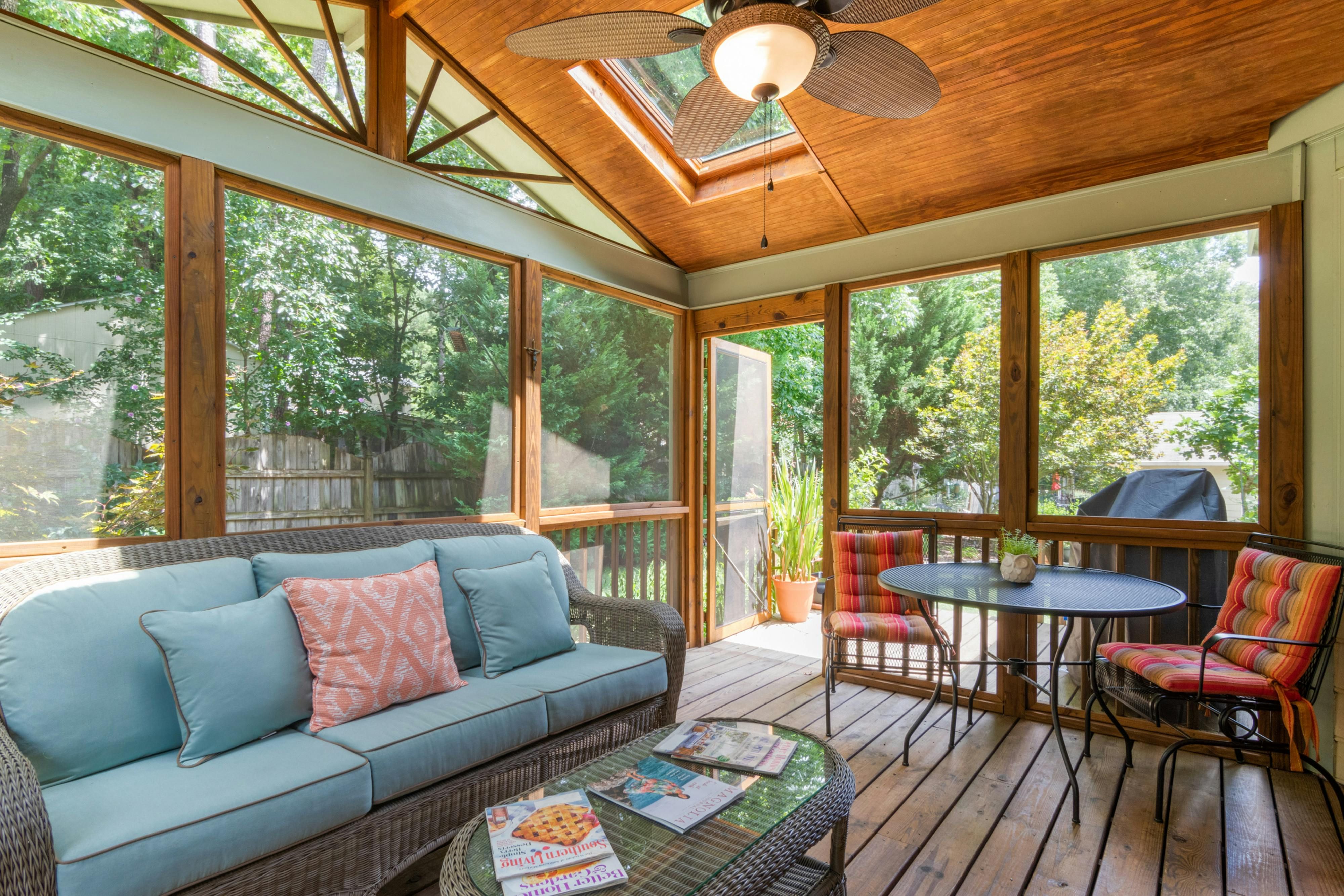 Sunlit patio scenery adorned with a cozy sofa, chairs, and a table, complemented by a lush potted plant and pillow-topped furnishings. Sunlit outdoor lounge featuring a sofa, chairs, and table, complemented by a potted plant and cushions adorning the furniture.
