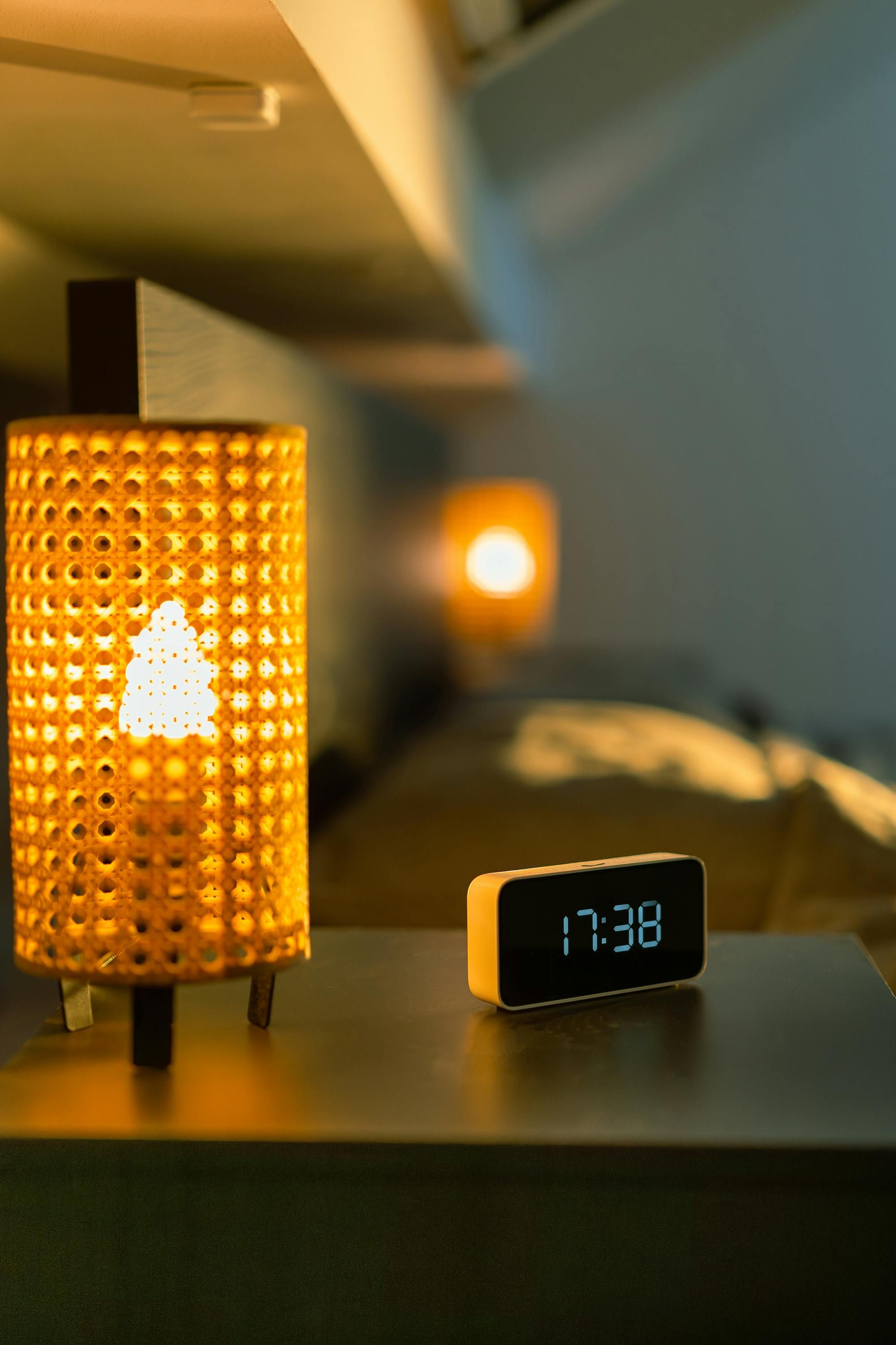 Table lamp resting on a nightstand, accompanied by an electric timepiece nearby. Table lamp positioned alongside a bed, featuring an electric timepiece clock nearby.