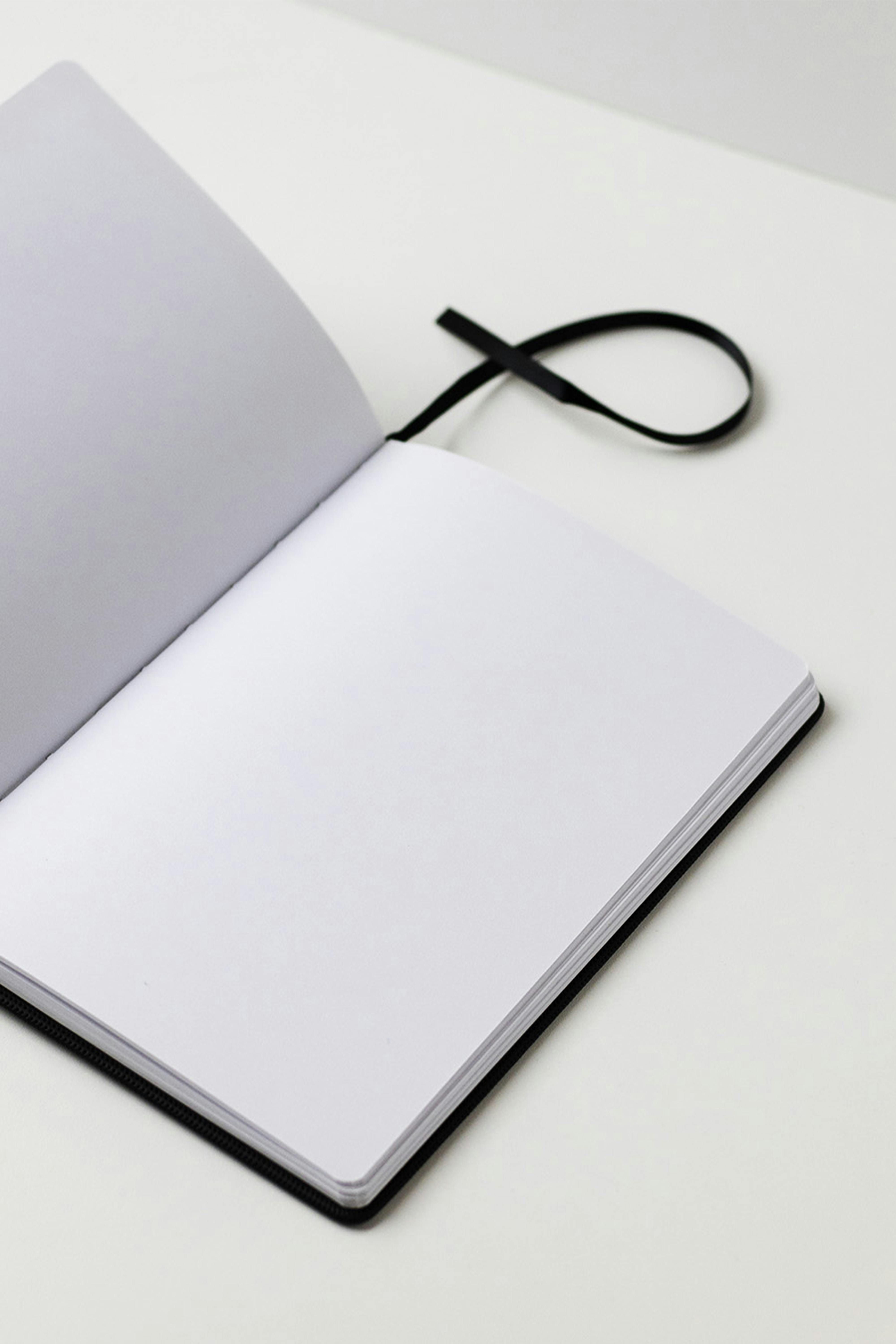 A spiral-bound notepad and a threaded bookmark embedded within it. Handwritten journal with a stitched page marker inserted